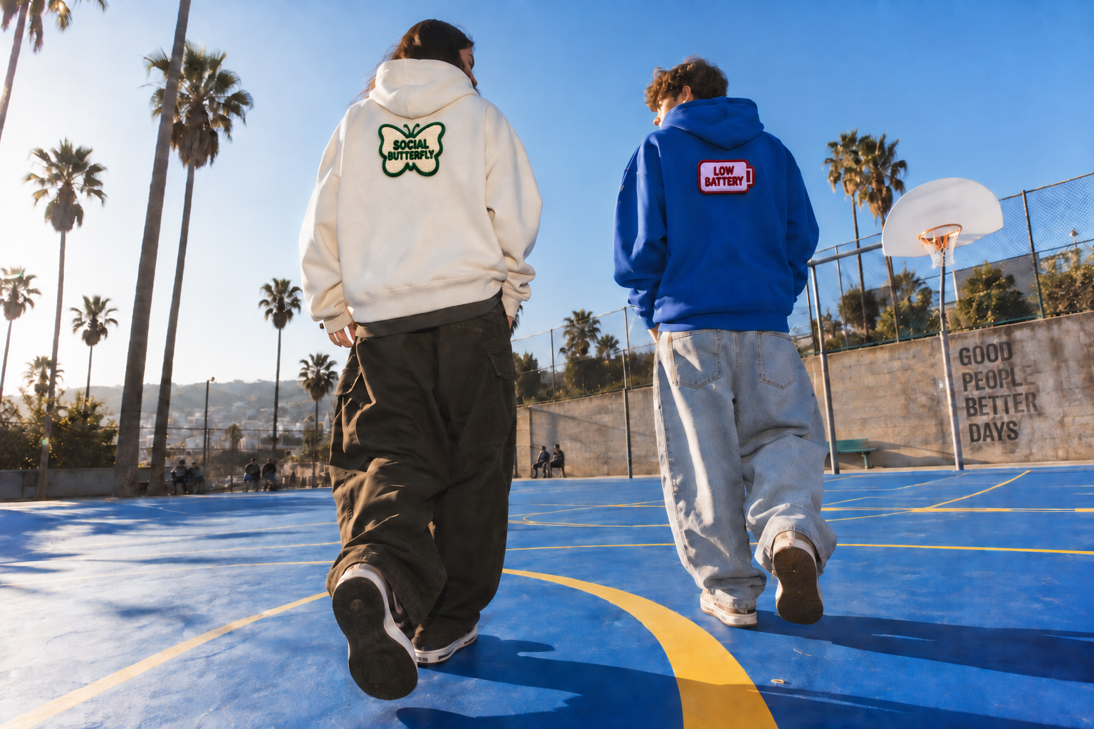 Two friends in cream and cobalt Moodie hoodies, with small Social Butterfly and Low Battery patches on the back